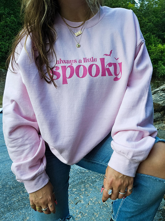 A girl wearing a pink Halloween crewneck sweatshirt that says "always a little spooky" in a bright pink, trendy font