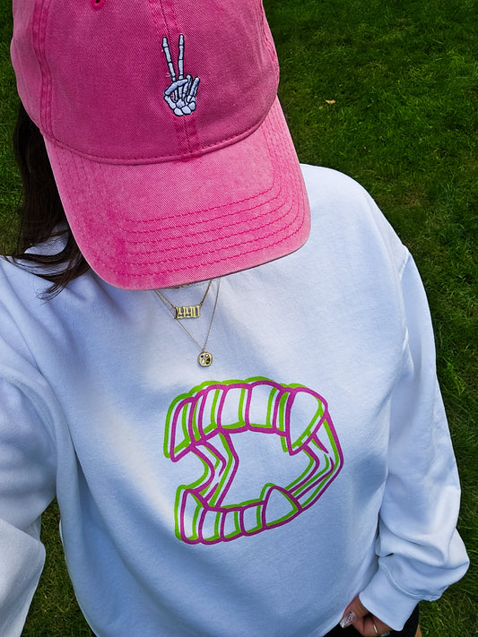 A girl wearing a white Halloween crewneck sweatshirt featuring an image of "glitch" style vampire teeth in pink and green