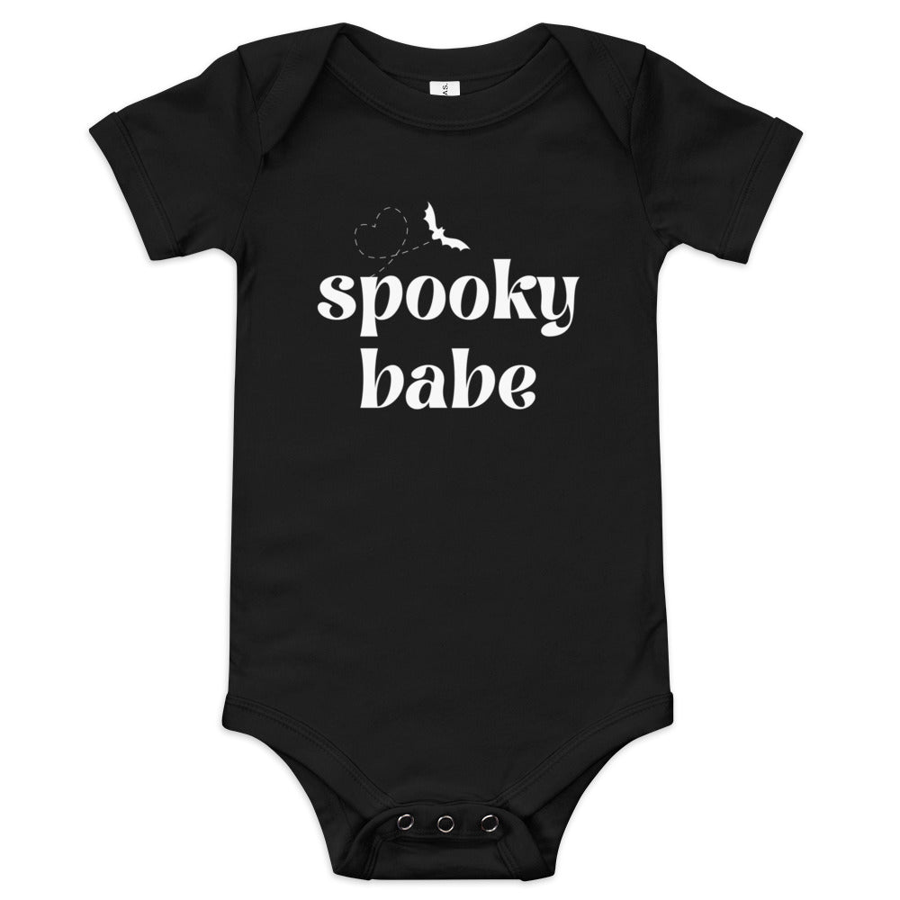 A black baby onesie that says "spooky babe" in a white retro font, with a bat flying in a heart-shaped pattern