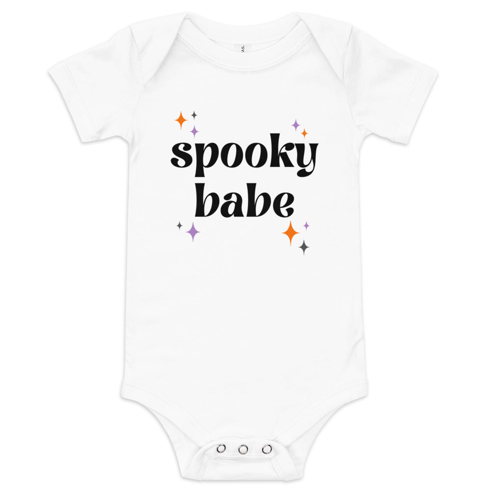 A white baby onesie that says "spooky babe" in a black retro font, surrounded by orange and purple sparkles