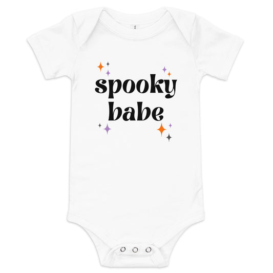 A white baby onesie that says "spooky babe" in a black retro font, surrounded by orange and purple sparkles