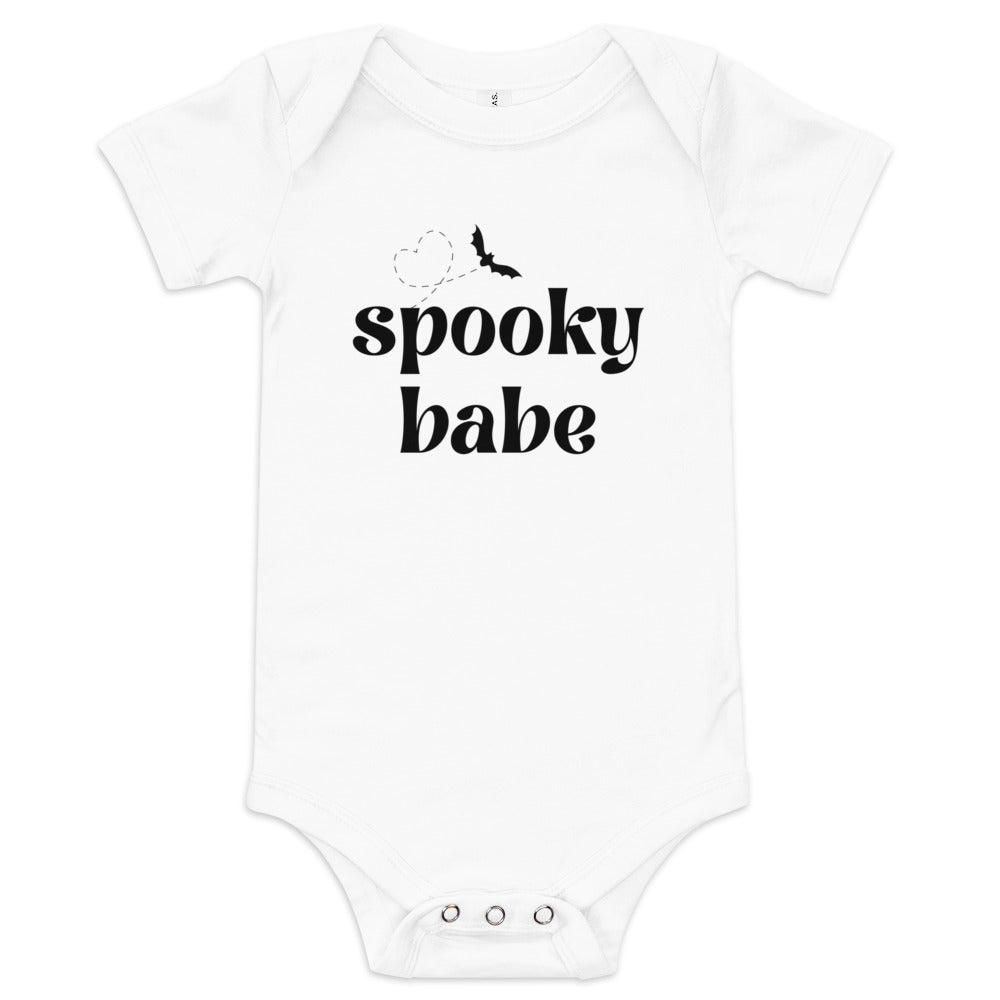 A white baby onesie that says "spooky babe" in a black retro font, with a bat flying in a heart-shaped pattern