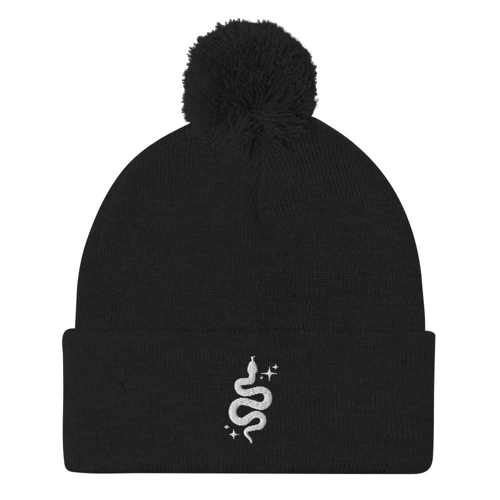 A black cuffed beanie with a pom-pom on top, featuring an embroidered snake and "sparkles"