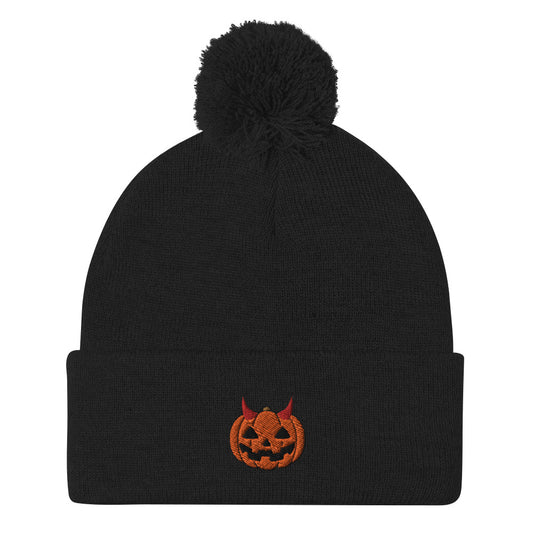 A black cuffed Halloween beanie with a pom-pom on top, featuring an embroidered jack-o-lantern wearing devil horns