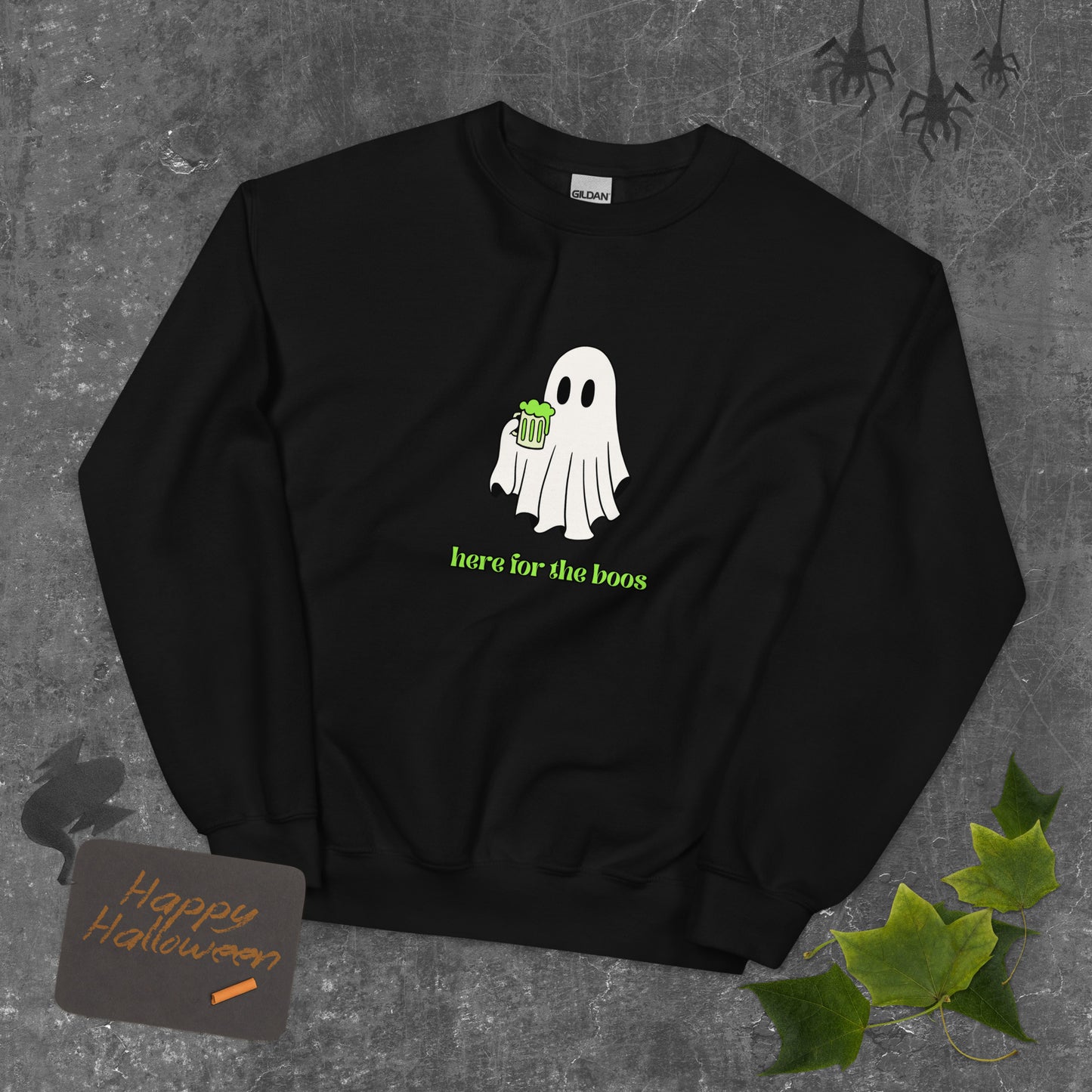 A black Halloween crewneck sweatshirt featuring a ghost holding a mug full of something green, with the phrase "here for the boos" underneath