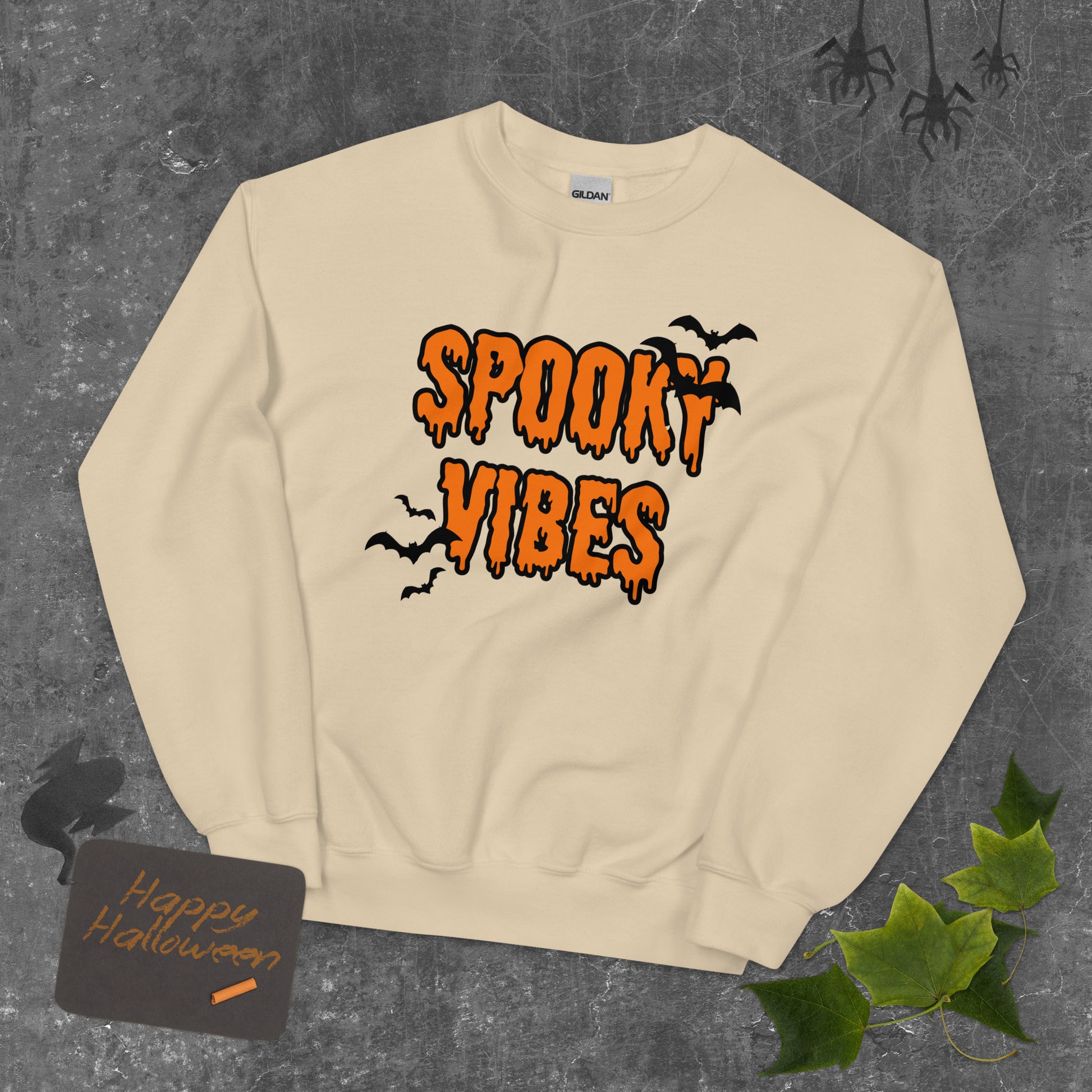 A tan Halloween crewneck sweatshirt that says "spooky vibes" in a creepy, dripping orange font, surrounded by bats