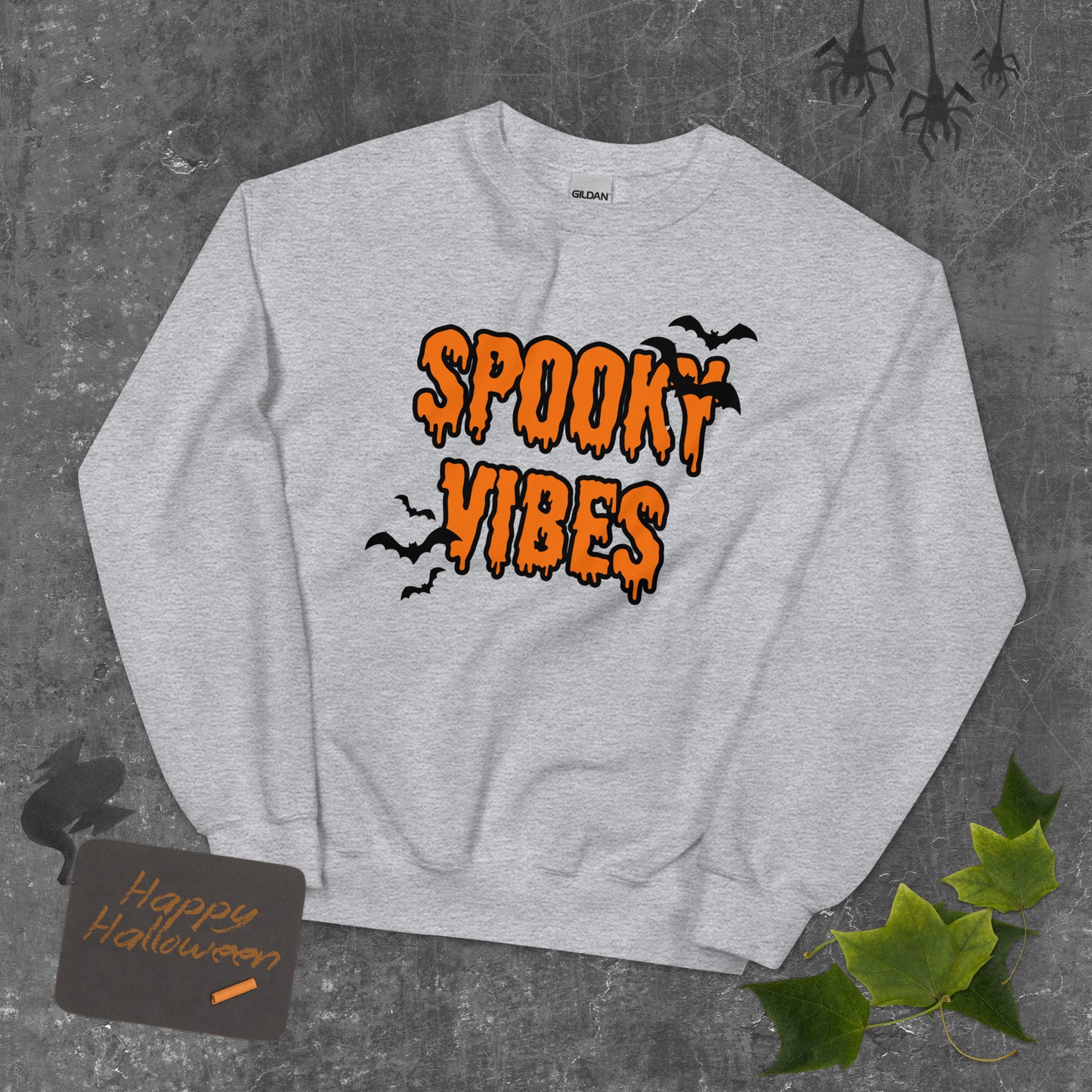 A gray Halloween crewneck sweatshirt that says "spooky vibes" in a creepy, dripping orange font, surrounded by bats