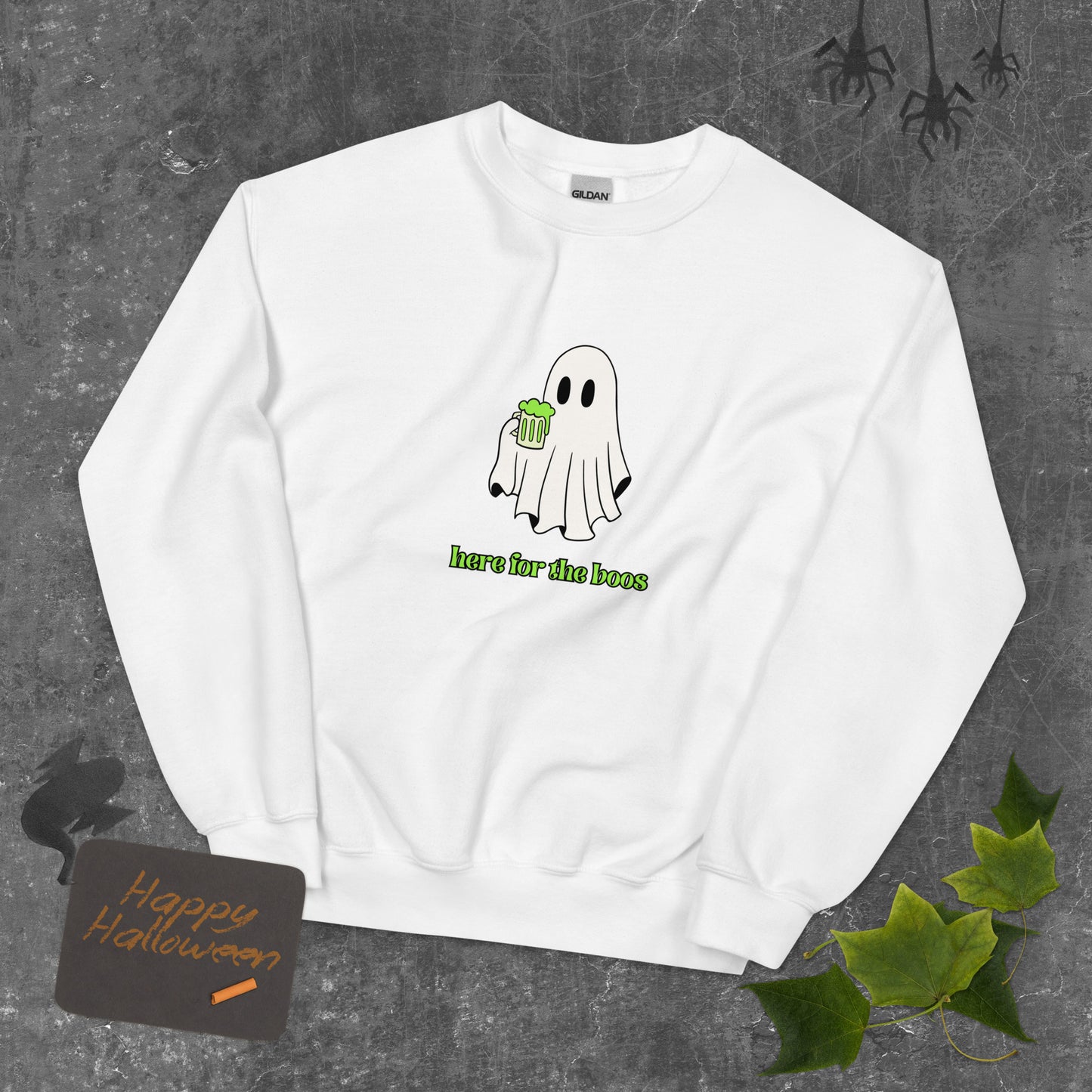 A white Halloween crewneck sweatshirt featuring a ghost holding a mug full of something green, with the phrase "here for the boos" underneath