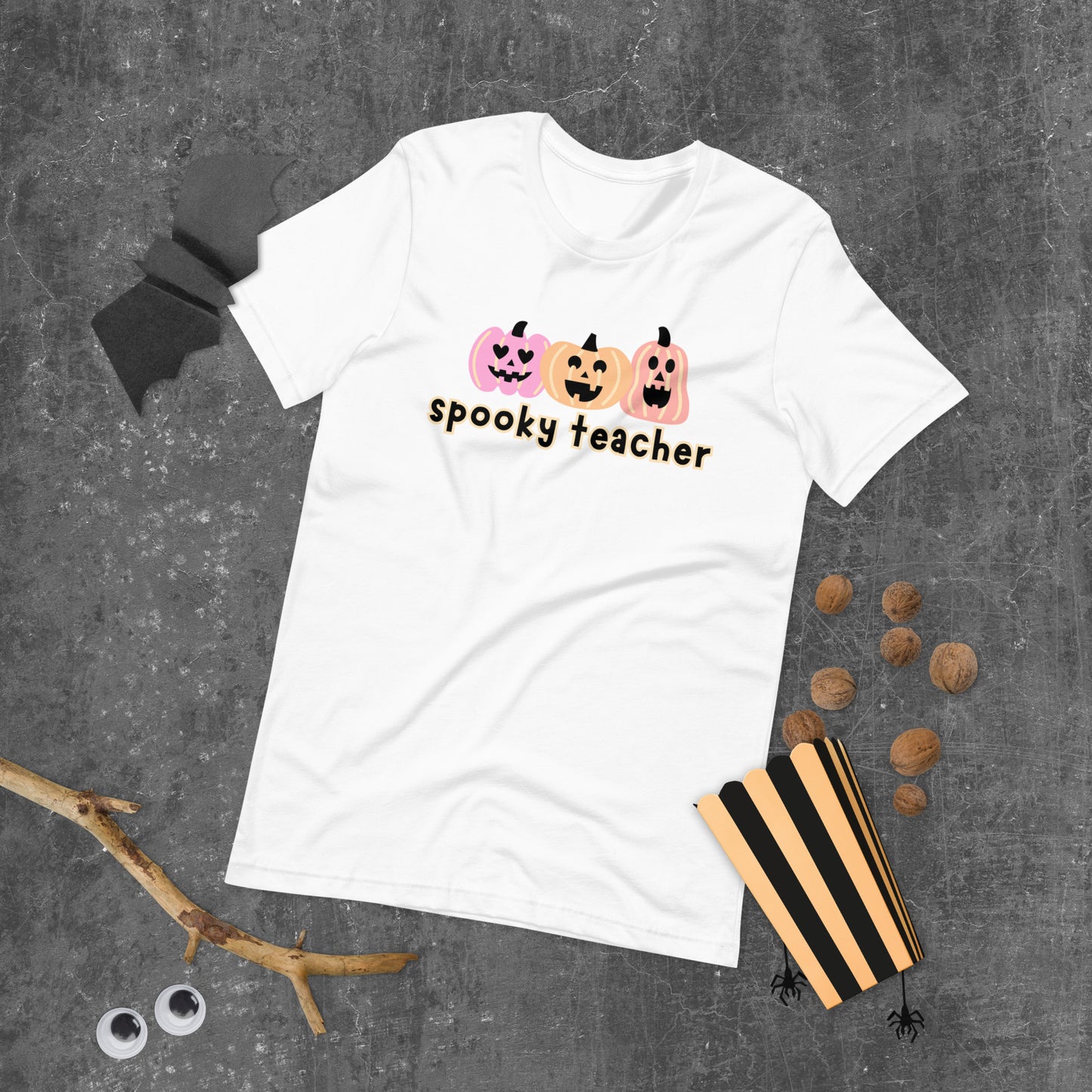 A white Halloween t-shirt featuring three pastel-colored pumpkins, with the phrase "spooky teacher" underneath