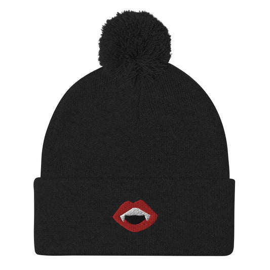 A black, cuffed pom-bom beanie with an embroidered mouth with red lips, white teeth, and fangs